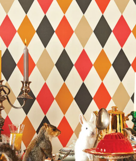Cole & Son Punchinello harlequin wallpaper in bold red, orange, black, and cream diamond pattern styled in an eclectic dining room setting.