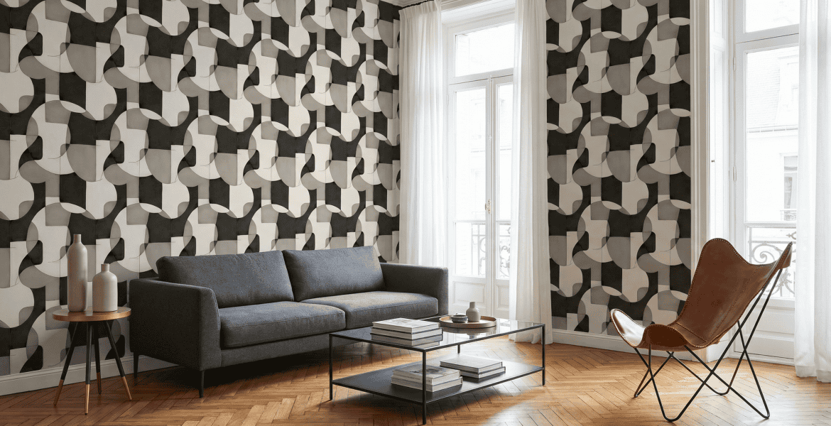A modern living room with bold geometric wallpaper, a grey sofa, and a brown leather butterfly chair.